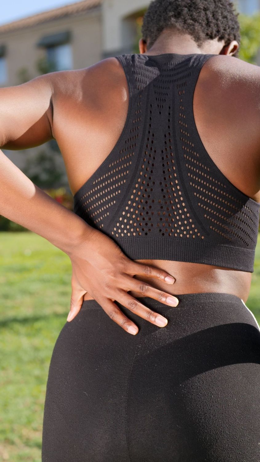 Mujer llevándose la mano a la zona lumbar mientras camina al aire libre